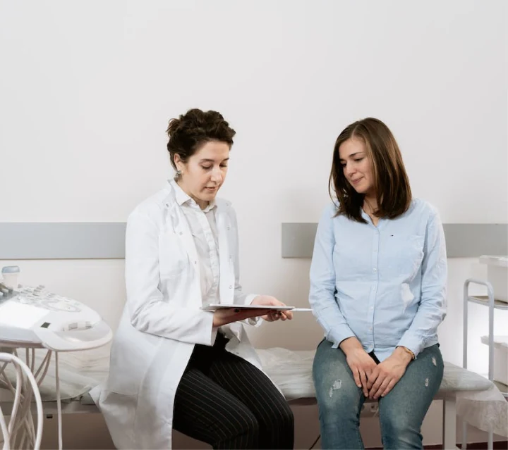 A doctor showing information on a clipboard to their patient while sitting inside an exam room.