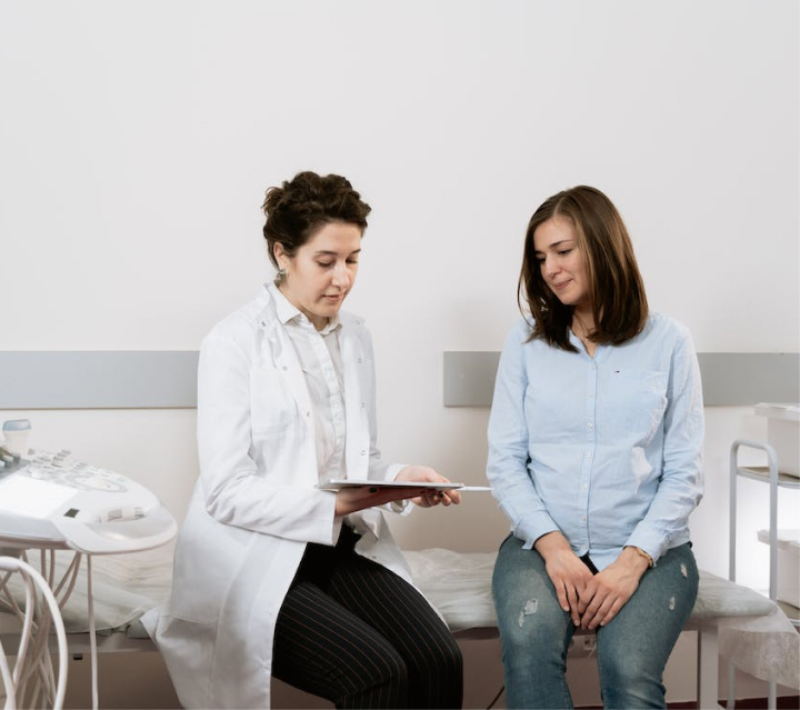 A doctor showing information on a clipboard to their patient while sitting inside an exam room.
