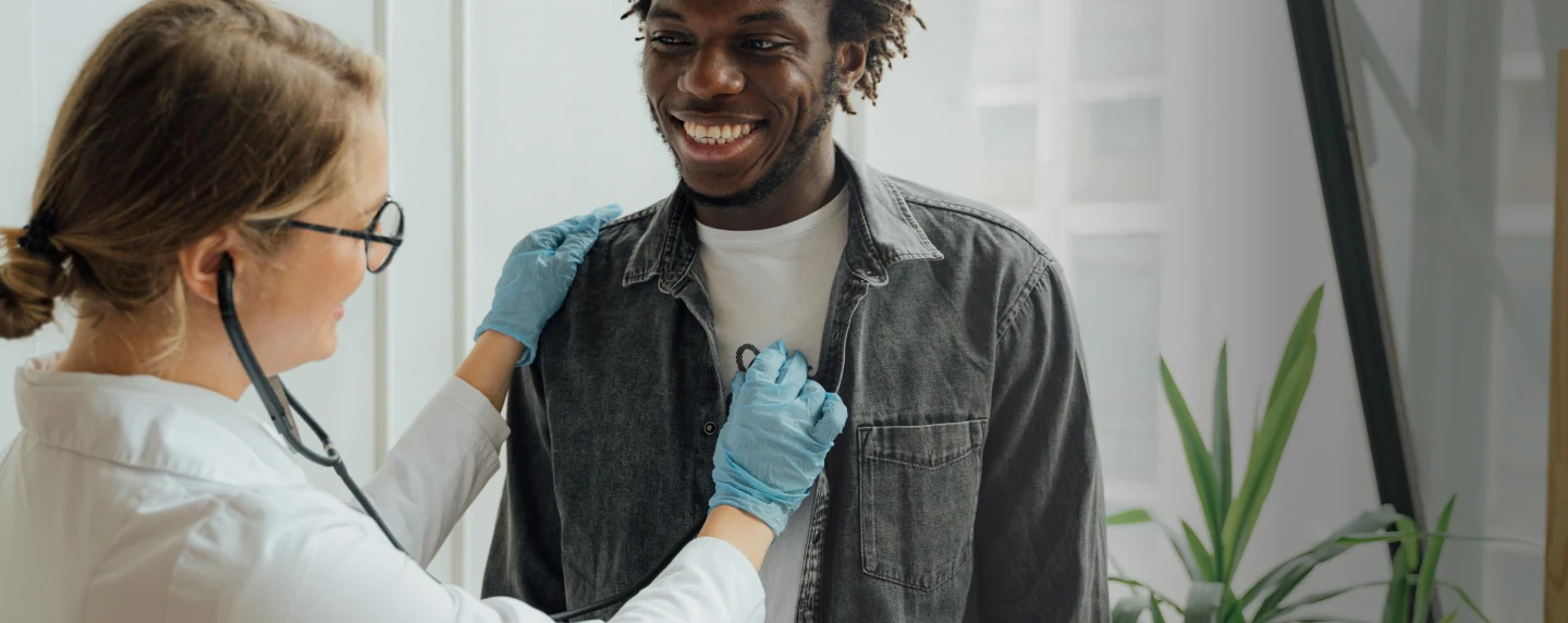 A healthcare professional listening to a smiling patient's chest with a stethoscope